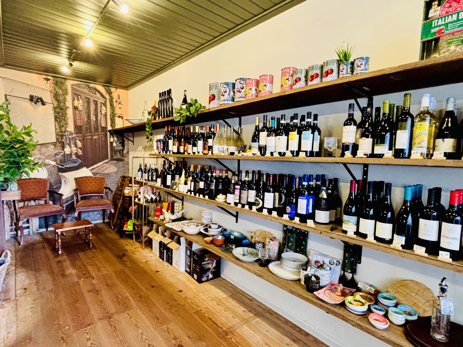 Het interieur van Holly's: planken vol wijn, schaaltjes en borden, een zithoek en een geschilderde Italiaanse straat op de muur